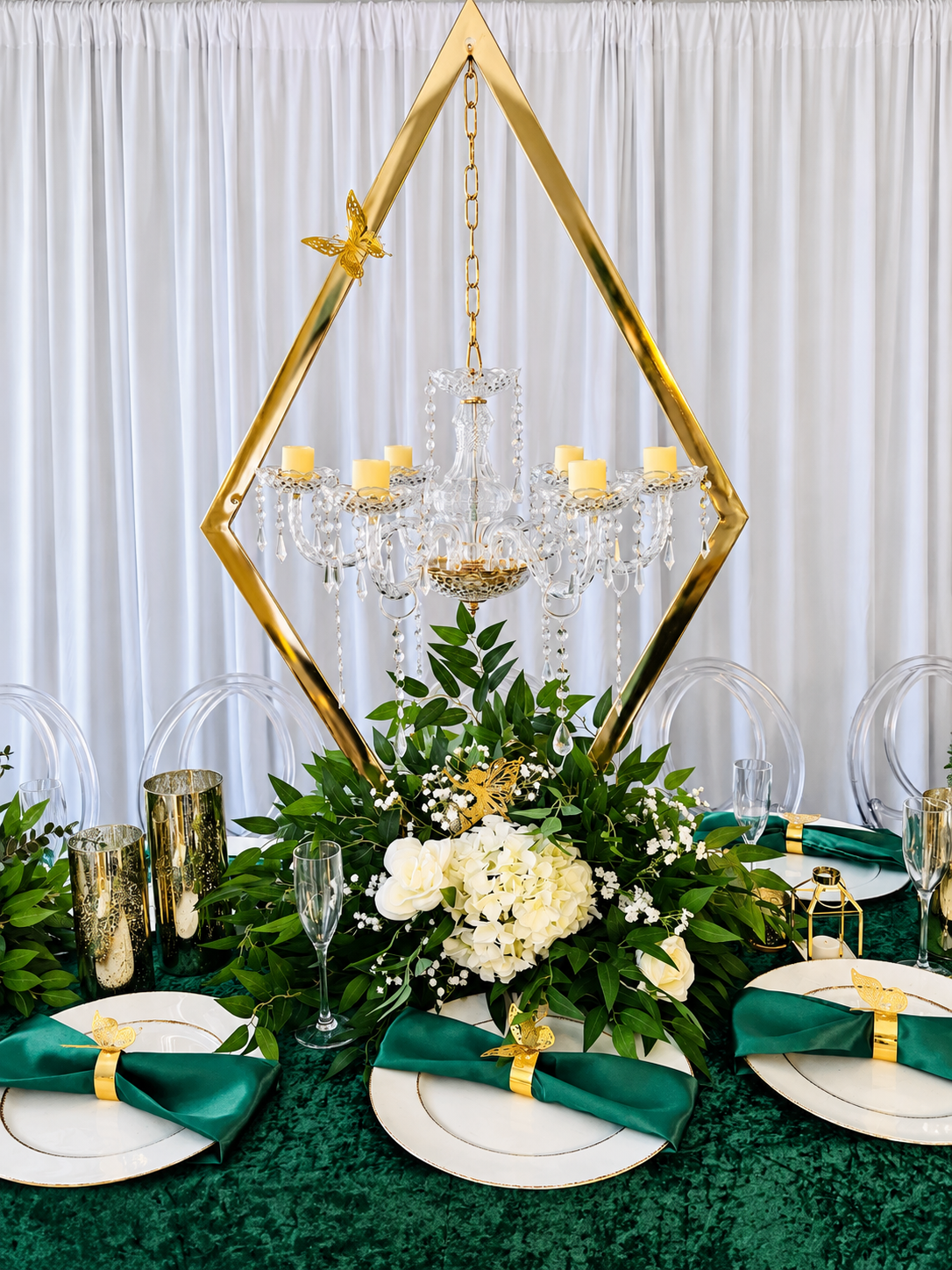 Emerald green and gold tablescape with white florals and a suspended crystal chandelier.